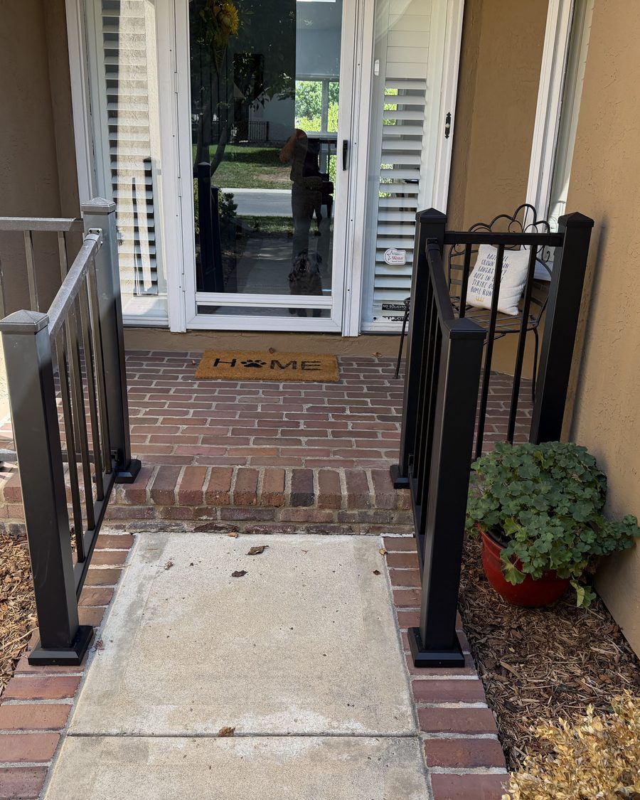 Powder-coated black aluminum handrail beside a brick front step